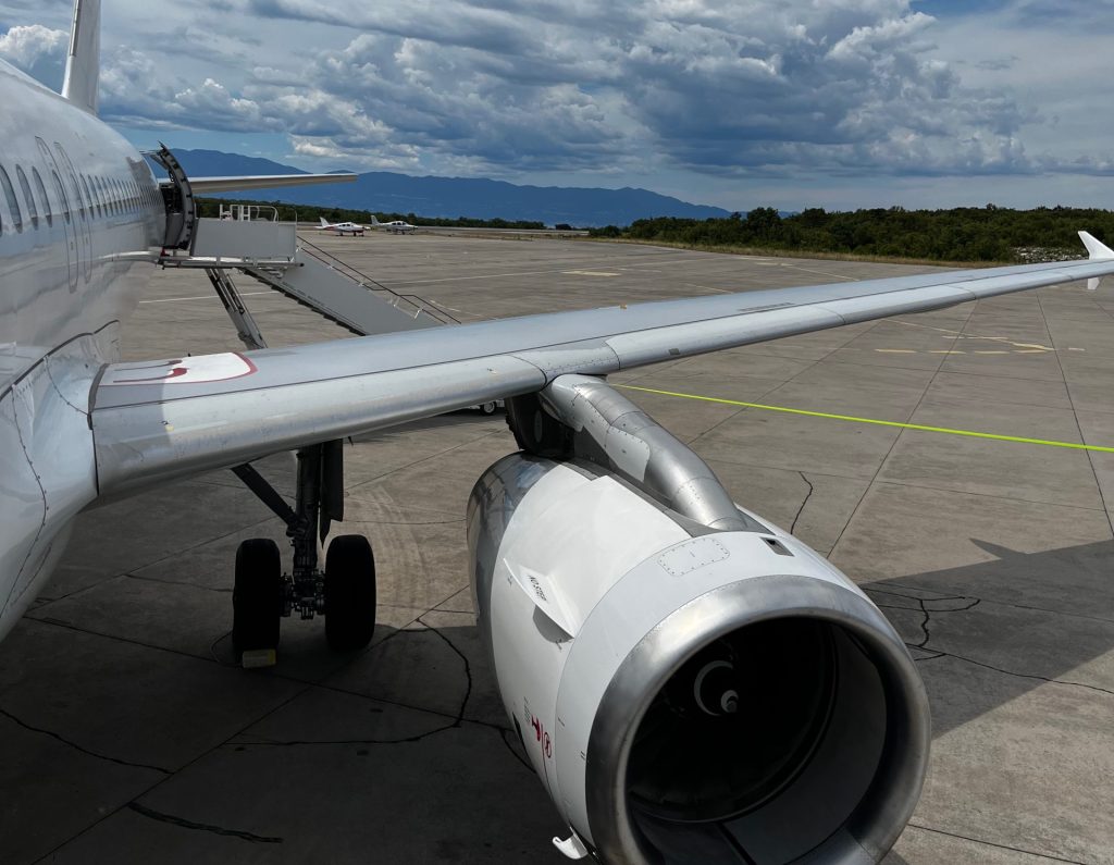 Airbus A320 parked on the ramp showing the CFM56 engine, right wing, and main landing gear with storm clouds in the background.